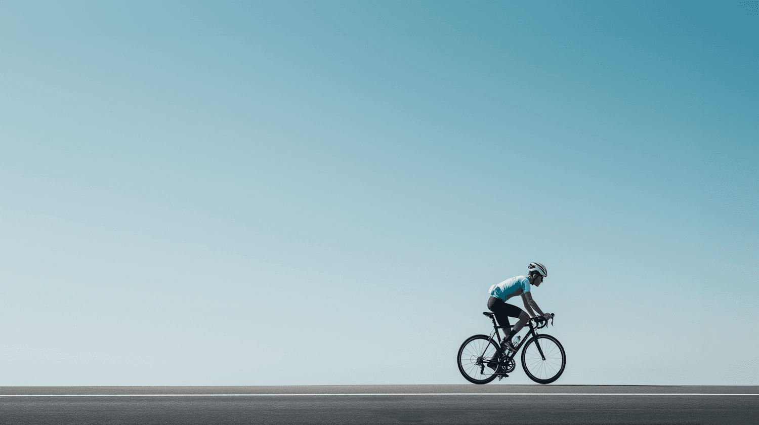 A road cyclist riding alone along a flat road under a clear blue sky